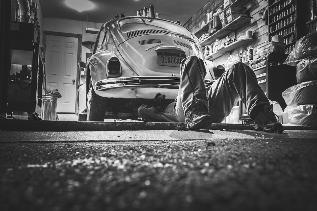 menu-03 Mechanic working beneath a classic Volkswagen Beetle in a vintage garage setting.