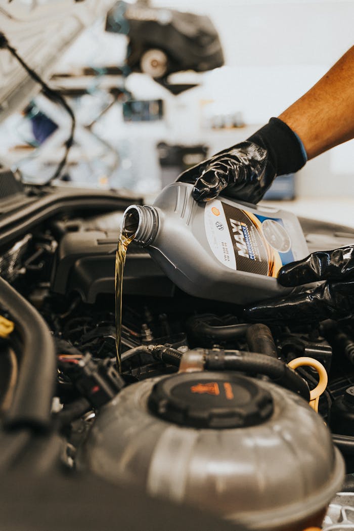 menu-12 A close-up of a mechanic in gloves pouring engine oil into a car engine, showcasing automotive maintenance.
