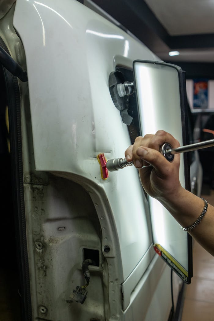 Close-up of vehicle dent repair in a garage using specialized tools under bright lighting.