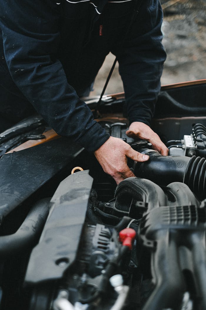 menu-13 Close-up of a mechanic's hands working on a car engine inside a workshop.