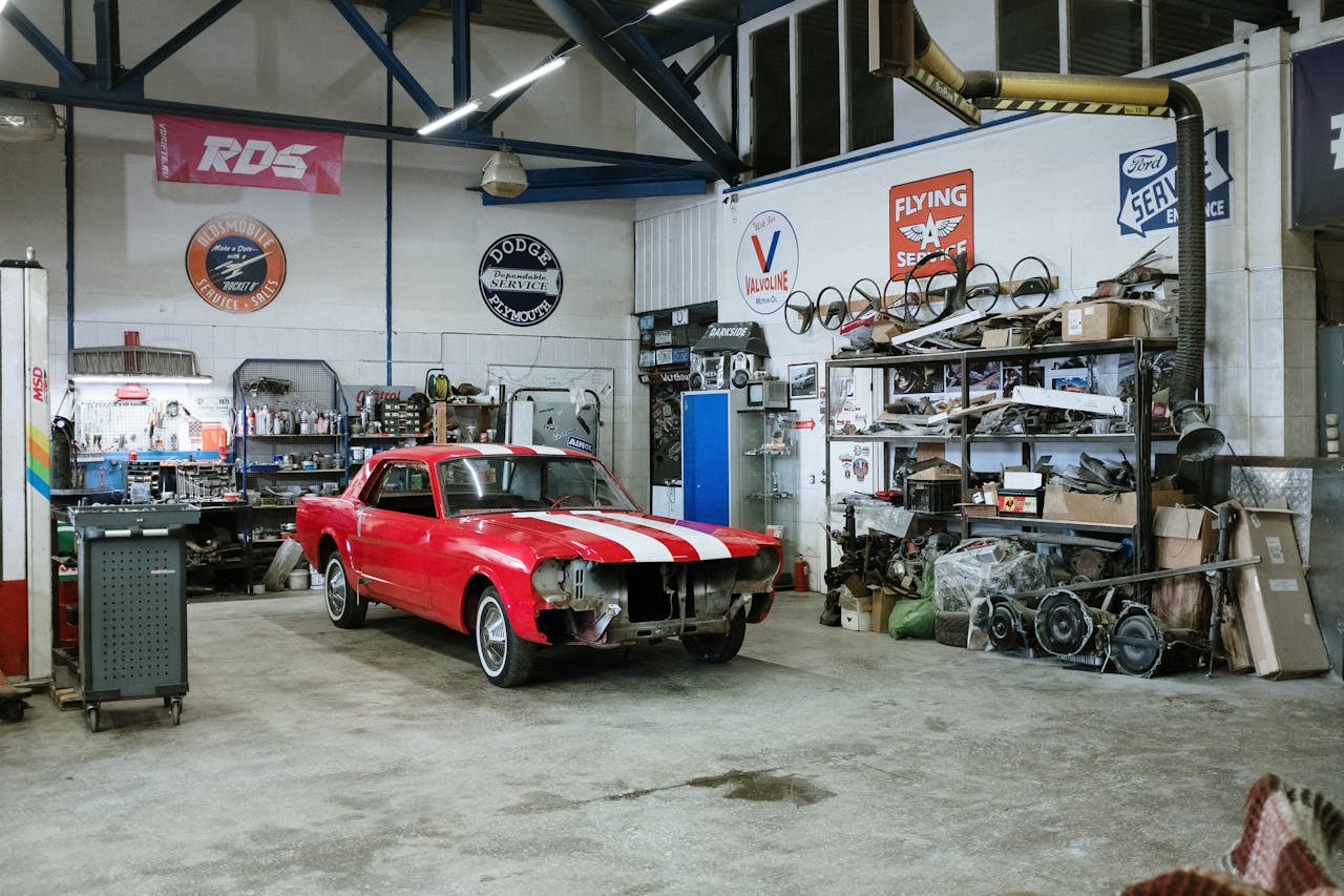 menu-15 A vintage red car undergoing restoration in a well-equipped workshop with various tools and auto parts.