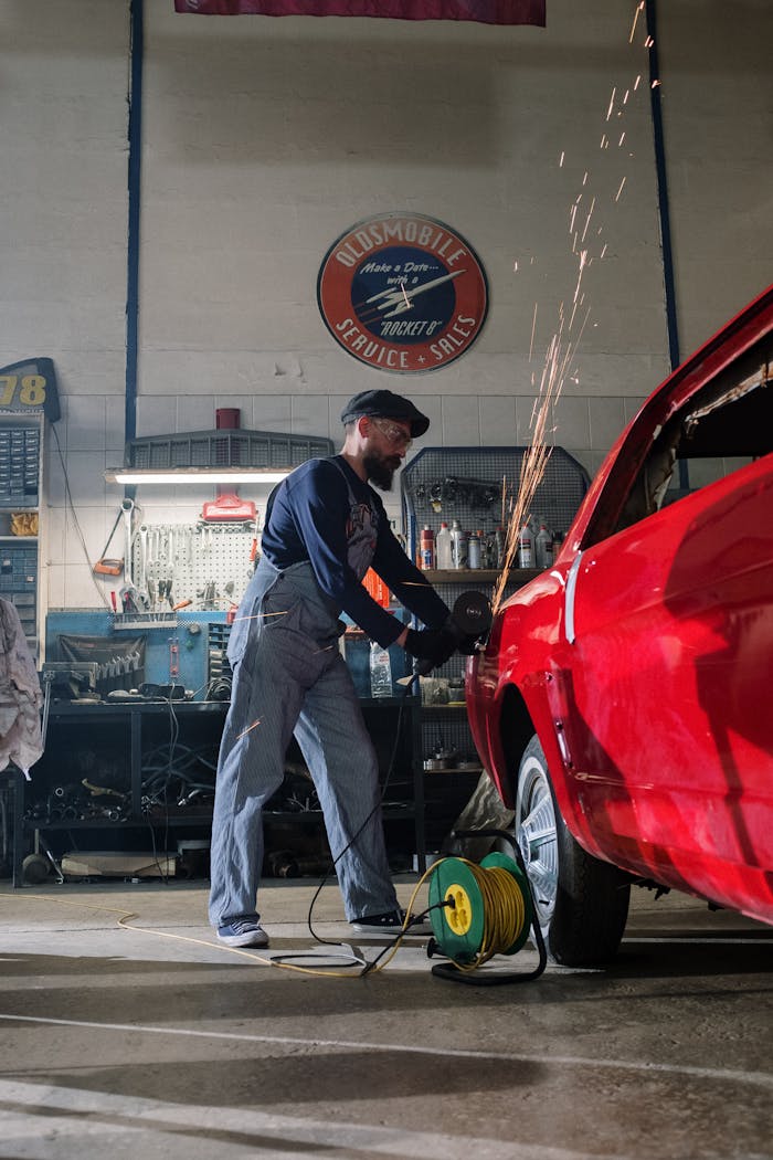 menu-06 Mechanic using grinder on car body in a busy garage, sparks flying as he works.