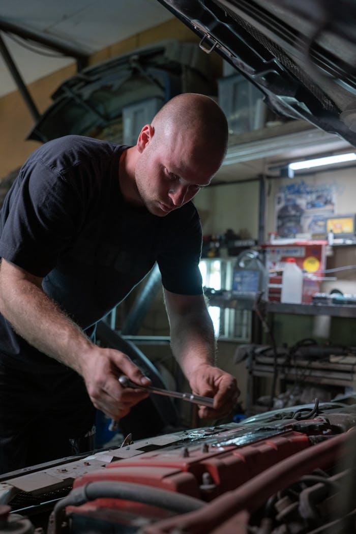 menu-14 A mechanic is diligently working inside a garage, fixing a car engine under the hood.