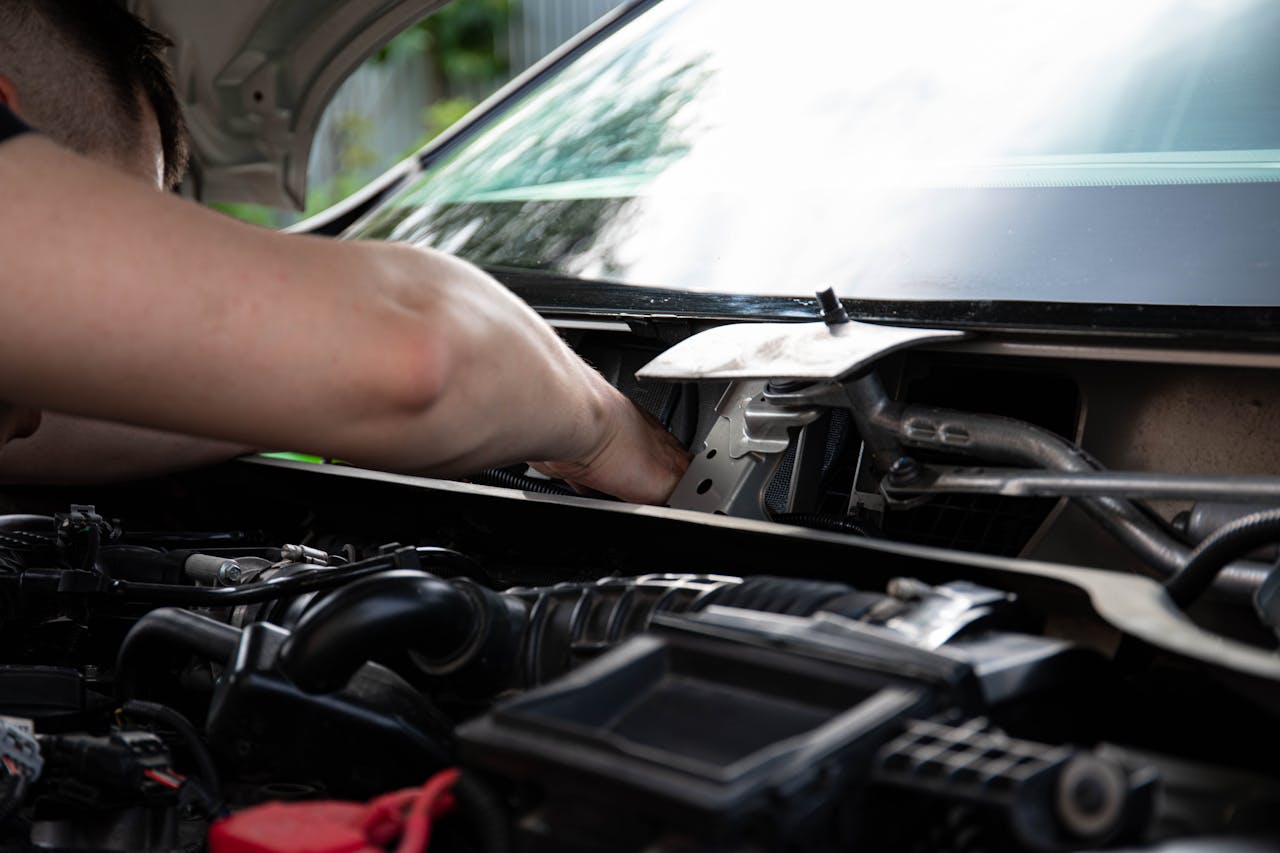 menu-04 Mechanic performing engine maintenance on a car outdoors, focusing on repair work.