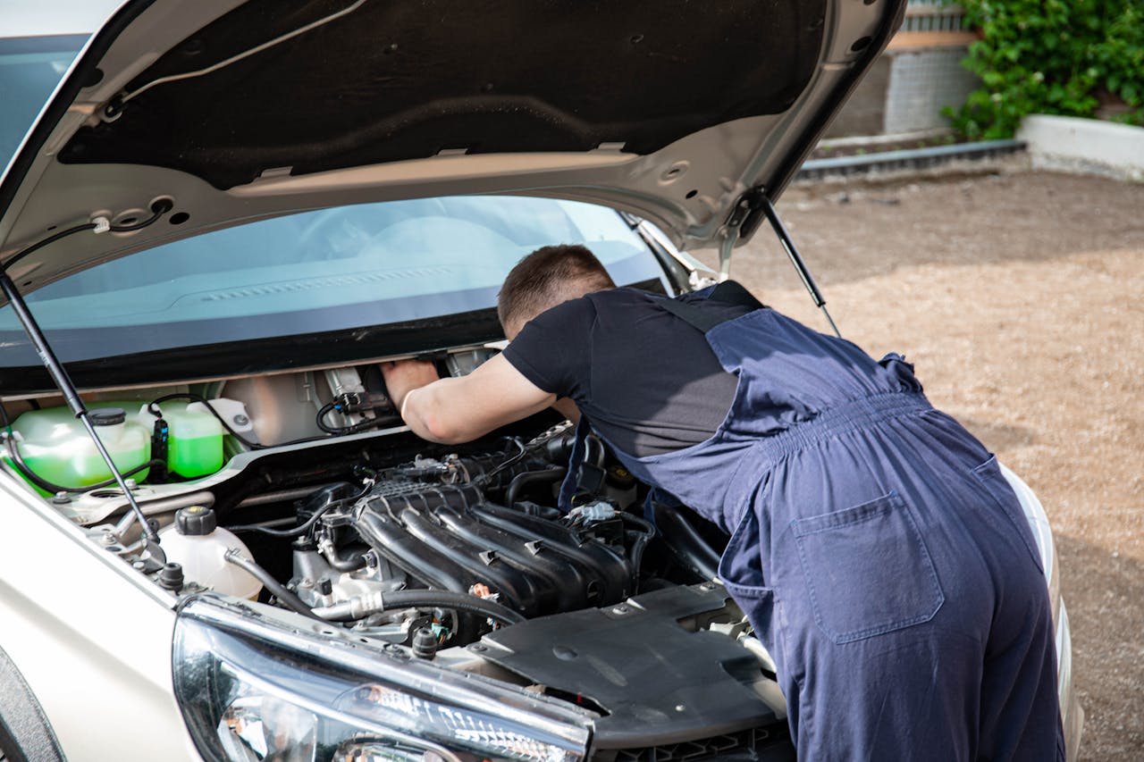 menu-10 Mechanic repairing car engine in daylight, showcasing technical skills.